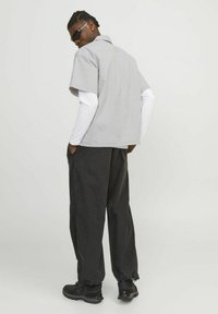 Grau Kurzarmhemd mit Kragen, kombiniert mit locker sitzenden schwarzen Hosen. Schwarze Sneakers mit elastischen Bündchen und Sonnenbrille runden den Look ab.