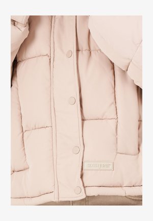 Helle beige Pufferjacke mit gestepptem Design, Druckknöpfen und einem Etikett mit der Aufschrift "SIXTH JUNE." Glatte Textur und abgerundete Ärmel.