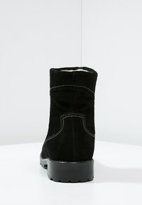 Bota de tobillo de ante negro con una suela negra texturizada y baja. Presenta un collar enrollado y costuras en contraste, que muestran un forro interior suave.