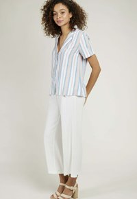 Chemise à manches courtes avec des rayures verticales multicolores, en tissu léger et avec une fermeture à boutons, associée à un pantalon large blanc court et à des talons beiges.