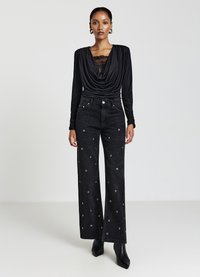 Schwarzes, drapiertes Oberteil mit Spitze und langen Ärmeln, kombiniert mit weiten schwarzen Jeans mit runden silbernen Verzierungen und hoher Taille.