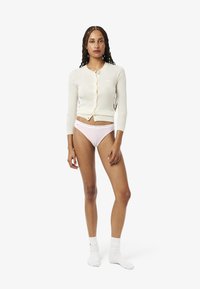 Geribbelde, crèmekleurige cardigan met lange mouwen en knopen, gecombineerd met roze slips en witte enkelsokken. Eenvoudig ontwerp zonder patronen.