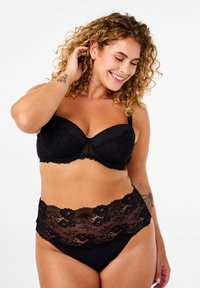 Reggiseno in pizzo nero con coppe lisce e fascia decorativa in pizzo. Lo slip a vita alta abbinato presenta pizzo trasparente e motivi floreali.