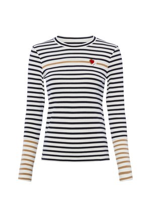 Chemise blanche à manches longues avec des rayures horizontales noires, une bande beige traversant la poitrine et les avant-bras, et un petit patch cœur rouge sur le côté supérieur gauche.