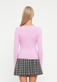 Haut à manches longues en maille côtelée de couleur rose pâle avec un col rond, associé à une jupe à carreaux noir et blanc avec une coupe évasée.
