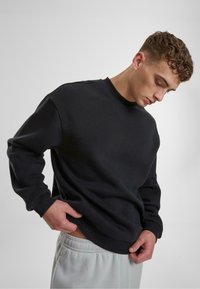 Schwarzer Rundhalsausschnitt-Sweatshirt in lockerer Passform, aus weichem Material gefertigt, mit gerippten Bündchen und Saum, kombiniert mit hellgrauen Jogginghosen.