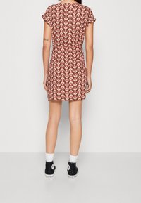 Short-sleeve dress with a geometric red and beige pattern, fitted waist, and a straight hem, paired with black high-top sneakers.