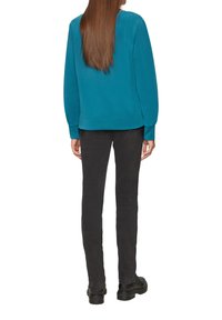 Teal sweatshirt met lange mouwen, ontspannen pasvorm en ribbelrand, gecombineerd met zwarte slim-fit broek en zwarte schoenen.