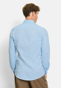 Hellblaues Langarmhemd mit einem kleinen Punktmuster, das einen spitzen Kragen und Knopfmanschetten besitzt, von hinten dargestellt.