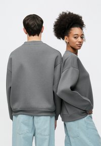 Gray fleece sweatshirt with a crew neckline and dropped shoulders, paired with light blue jeans. Smooth texture, minimal detailing.