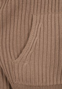 Gros plan sur un tissu en maille côtelée marron avec un motif texturé vertical et un détail de couture courbée.