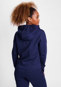 Donkerblauwe hoodie van zacht materiaal, met een relaxte pasvorm, geribde manchetten en een kangoeroe-pocket aan de voorkant.