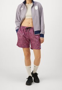 Purple zip-up jacket with navy accents, beige crop top, pink leopard print shorts with drawstring, white socks, and black sneakers.