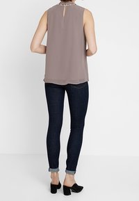 Blouse sans manches mauve avec un dos en trou de serrure et un ourlet transparent, associée à un jean en denim foncé et des mules noires à talons carrés.