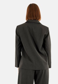 Blazer grigio scuro con righe sottili, dalla vestibilità sartoriale, maniche lunghe e rever a scollo a V, abbinato a pantaloni coordinati, mostrando un tessuto textured.
