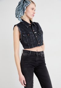 Mustmust denim cropitudel koos frakitud servadega, kahe eesmise tasku ja pruunide nööpidega. Kantud mustade kõrge vöökohtadega teksade üle; mudelil on seljas ruuduline peapael.