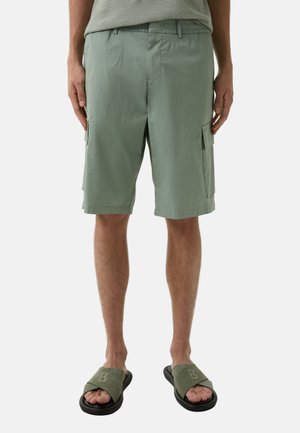 Light green cargo shorts made of lightweight fabric, featuring side pockets, an elastic waistband, and a relaxed fit. Paired with green sandals.