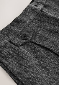 Gewebestoff mit Fischgrätmuster in Schwarz und Grau, mit Klappentasche und schwarzen Knöpfen, mit weicher, strukturierter Oberfläche.