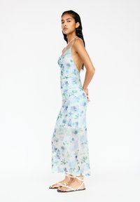 Hellblaues Maxi-Kleid mit floralen Mustern, figurbetontem Schnitt, dünnen Trägern und transparenter Textur. Akzentuiert mit zarten blauen Blumenmustern.
