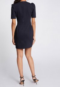 Marineblaues Kleid mit kurzen Puffärmeln, figurbetonter Form, Rückenreißverschluss und glatter Textur; kombiniert mit schwarzen, strappy High Heels.