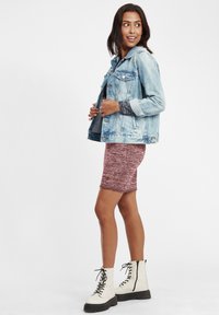 Lyseblå denimjakke, tettsittende design, iført over en mørk bordo skjøt. Modell i hvite snøresandaler. Glatte teksturer og uformell stil.