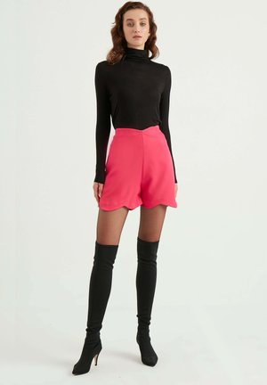 Un col roulé noir, un short rose à bord festonné, des bottes noires montantes. Texture lisse, design ajusté, couleurs contrastées. Aucuns motifs ni éléments métalliques visibles.