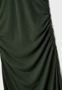Tissu de robe vert foncé avec une texture plissée, présentant des drapés doux et des détails de ruché sur le côté pour une dimension supplémentaire.