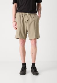 Beige fleece shorts with an elastic waistband and drawstring, featuring two side pockets and a relaxed fit, paired with black sneakers.