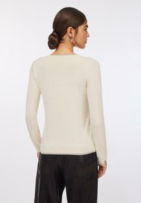 Maglione beige chiaro a maniche lunghe con scollo rotondo e design aderente. Tessuto liscio, spacchi laterali all'orlo e polsini a coste.