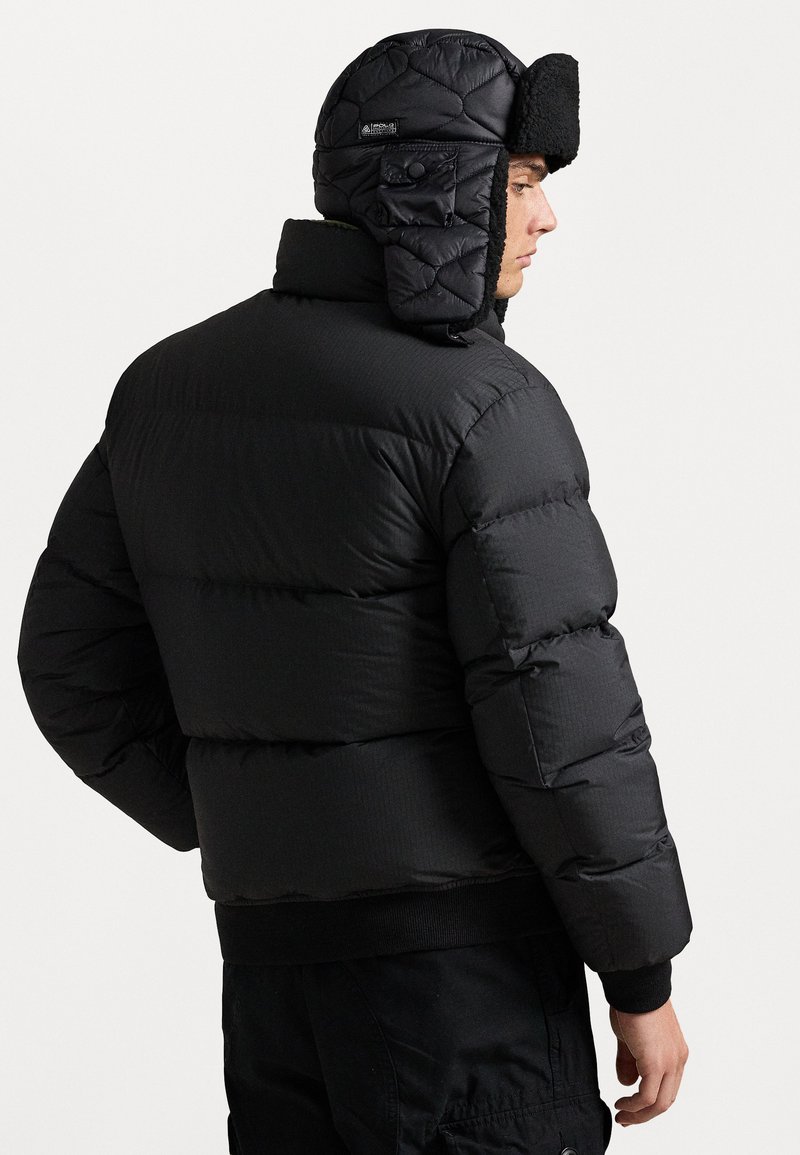 Zwarte pufferjack met geribde manchetten en zoom, met een doorgestikt textuur en een vastgemaakt zwart oorflaphoed met een harige voering.