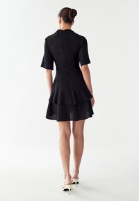 Vestido negro de capas con cierre de cremallera en la parte posterior, mangas cortas y una falda fluida. Tela suave con un aspecto ligero.