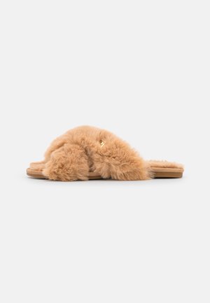 Yksittäinen vaaleanruskea slip-on-sandaali, jossa paksut, pehmeät karvaiset remmit ja litteä pohja valkoisella taustalla.