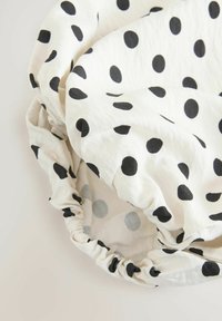 Sac ou housse en tissu blanc à pois noirs avec un bord élastique froncé, présenté froissé sur un fond neutre.