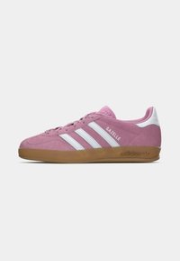 Pink ruskindssneakers med hvide læderdetaljer, der har tre hvide striber, en tekstureret tunge og en gummirubsål. Stylet som "Gazelle."