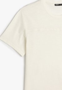 T-shirt color crema realizzato in morbido tessuto, con scollatura a girocollo e maniche corte, caratterizzato da un sottile dettaglio di cucitura orizzontale.