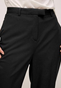 Pantalons noirs ajustés en tissu lisse, avec une taille plate, des poches latérales discrètes et un design de ceinture épuré.