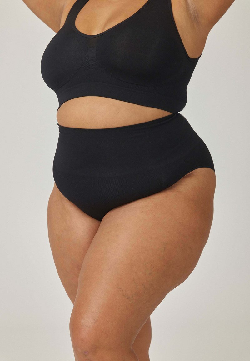 Czarny zestaw odzieży sportowej z bezszwowym biustonoszem z wycięciami i szortami z wysokim stanem. Gładka tekstura i dopasowany krój.