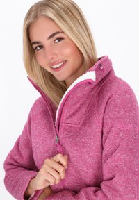 Fleece jakna v heather roza barvi z zadrgo, visokim ovratnikom in belim puhastega obloga. Ima našite detajle in žep.