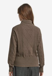 Brun stickad tröja med hög krage, med kabelstickade och diamantmönster. Ribbad mudd och nederkant ger textur till designen.