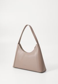 Borsa a mano in pelle beige con manico curvo, forma angolare, chiusura con zip in alto e logo embosso discreto sul davanti. Texture liscia su tutta la superficie.