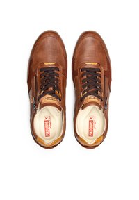 Sneaker in pelle marrone con un design testurizzato, lacci neri e una cerniera laterale. Le sole interne mostrano un logo su uno sfondo crema.