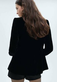 Sort fløjl blazer med lange ærmer, skræddersyet pasform og en glat tekstur. Ryggen har en diskret flair og et rent, minimalistisk design.