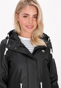 Czarna wodoodporna kurtka z kapturem, białymi sznurkami i srebrnymi elementami. Posiada małe logo parasolki na klatce piersiowej oraz pasek w poziome paski pod spodem.