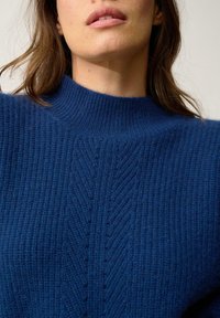 Niebieski sweter dzianinowy z wysokim kołnierzem, z fakturowanym wzorem i pionowymi prążkami, wykonany z miękkiego, grubego materiału.