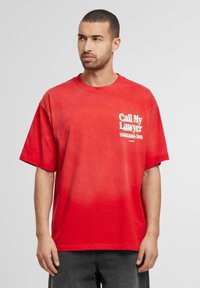 Rød oversized T-shirt lavet af bomuld med korte ærmer. Har hvid tekst "Ring til min advokat" og et telefonnummer på venstre bryst.