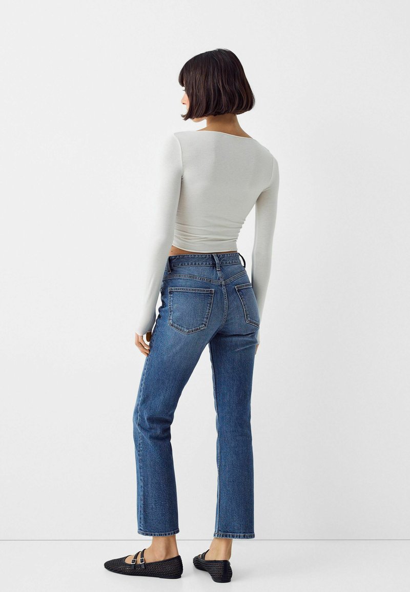 Maglietta grigia chiara a maniche lunghe, jeans blu scuro a vita alta con vestibilità dritta e ballerine nere intrecciate. Design minimale con tasche posteriori.