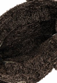 Brauner, strukturierter, flauschiger Stoff im Inneren einer Tasche mit sichtbarem Reißverschluss und Kettendetail. Ausgekleidet mit weichem, dunklem Material.