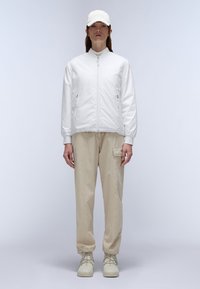 Witte bomberjack met rits, beige cargobroek met zijzakken, en lichtgekleurde sneakers op een neutrale achtergrond.