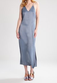 Vestido midi de satén gris con escote en V y tirantes finos, con una abertura lateral. Combinado con sandalias de tacón bloque metálicas.