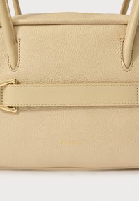 Τσάντα χειρός από δέρμα σε μπεζ με υφή, με δομημένο σχήμα, χρυσά μεταλλικά στοιχεία και ανάγλυφο το όνομα του brand στην μπροστινή πλευρά.